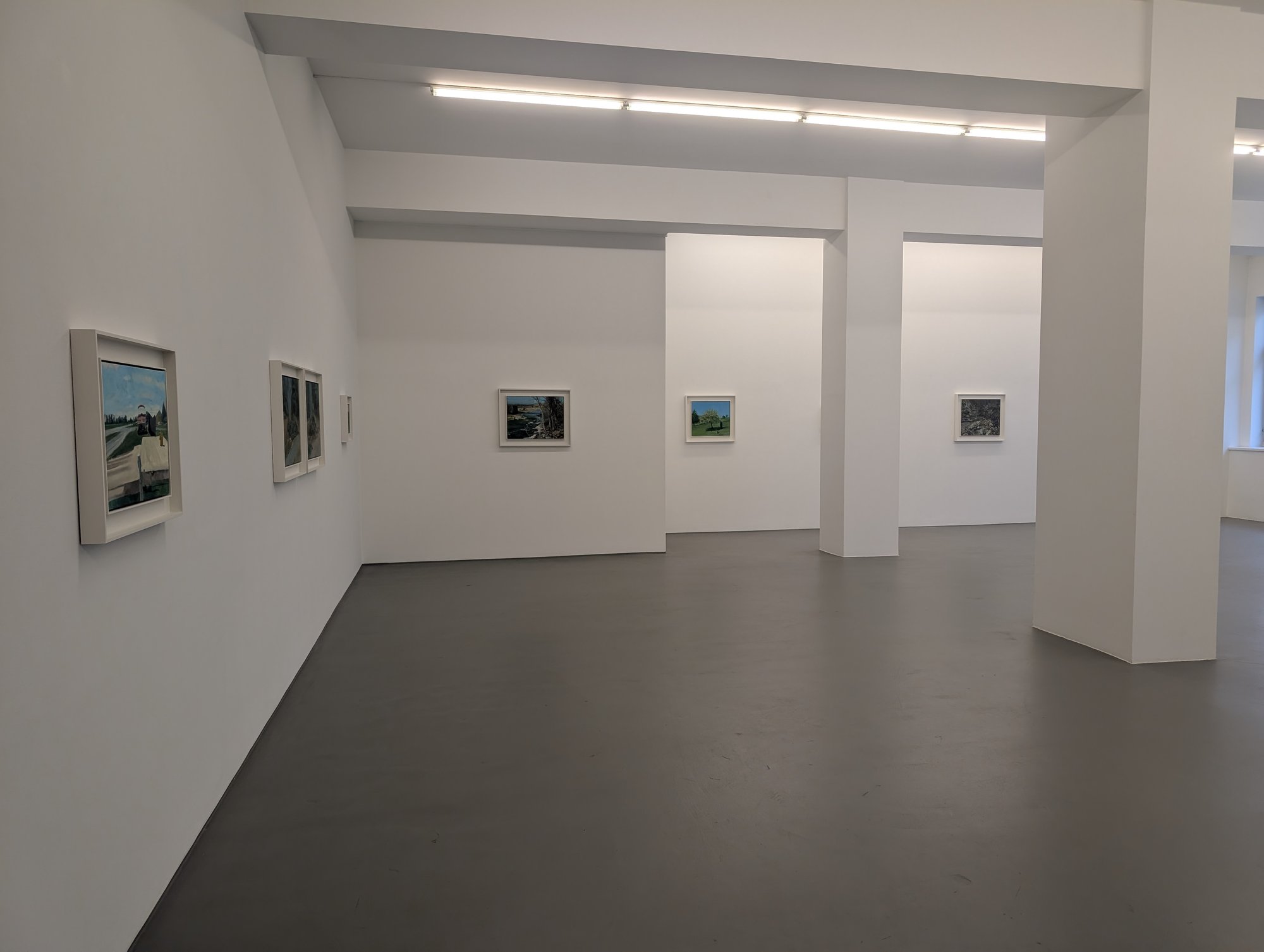 Kleinformatige Bilder in tiefen weißen Kastenrahmen im großen weißen Saal, zweite Station des Rundgangs